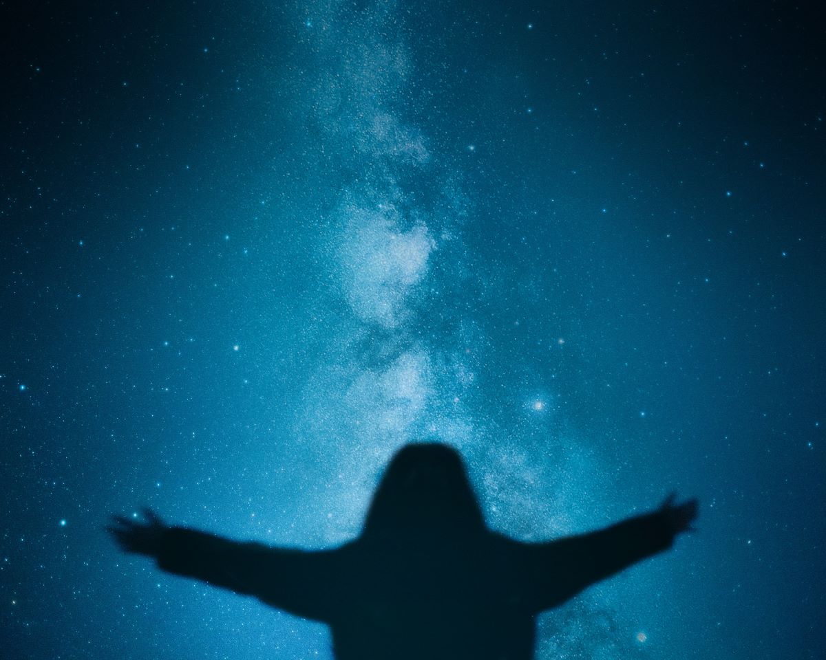 Silhouette of a person spreading their arms while facing the starry indigo sky