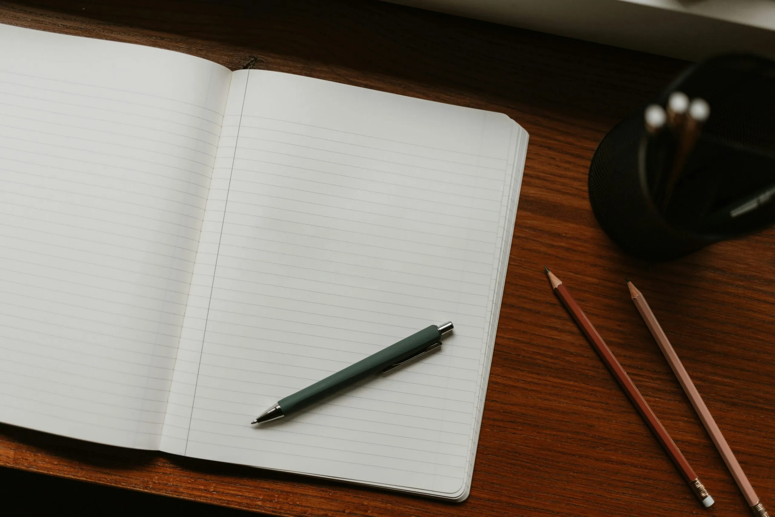 Open notebook with pen on a wooden desk beside pencils, symbolizing journaling, reflection, and recording thoughts