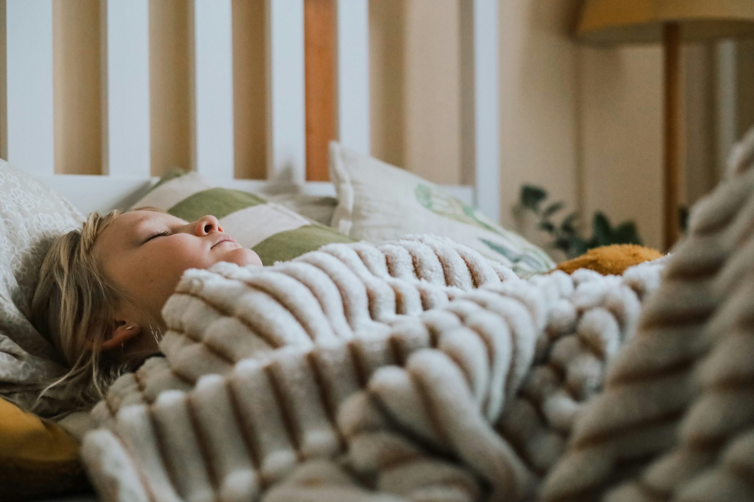 Child sleeping peacefully under a soft blanket, resting comfortably in a cozy and warm bedroom setting.