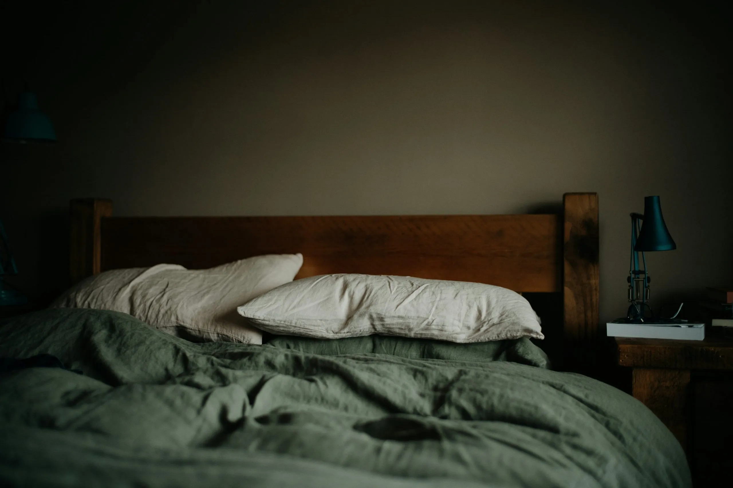 Unmade bed with pillows and bedside lamp in dimly lit room, symbolizing sleep and dreaming