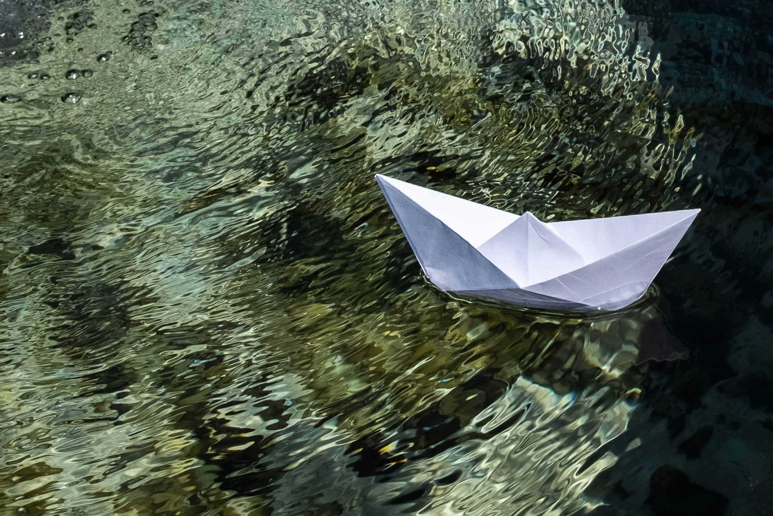 Paper boat floating on rippling water, symbolizing journey, emotions, and fragile dreams