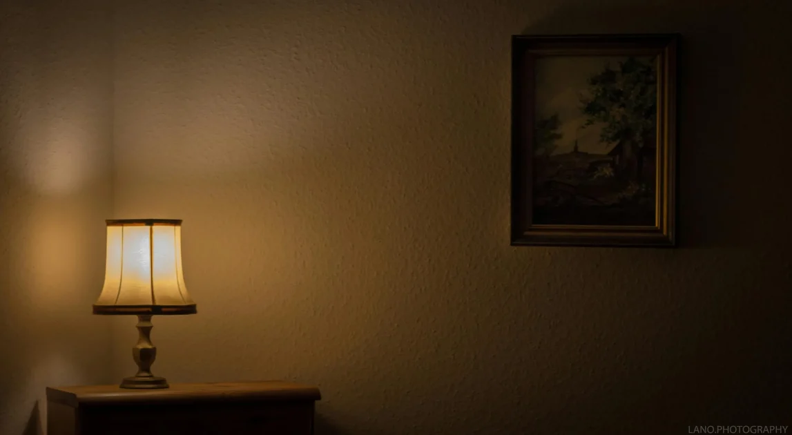 Warm bedside lamp glowing in a dim room with a framed picture, creating a calm and reflective nighttime atmosphere