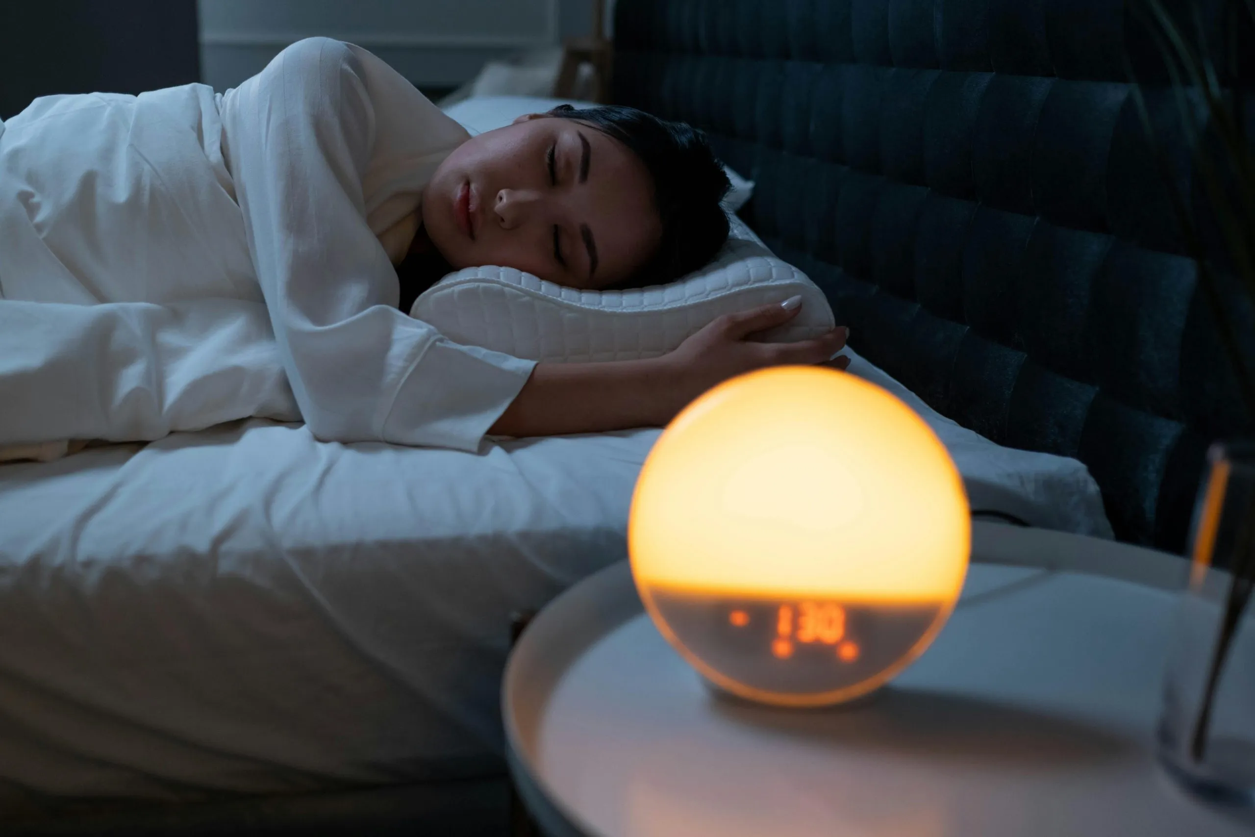 Woman sleeping peacefully at night with a glowing alarm clock lamp beside the bed, symbolizing rest and sleep routine