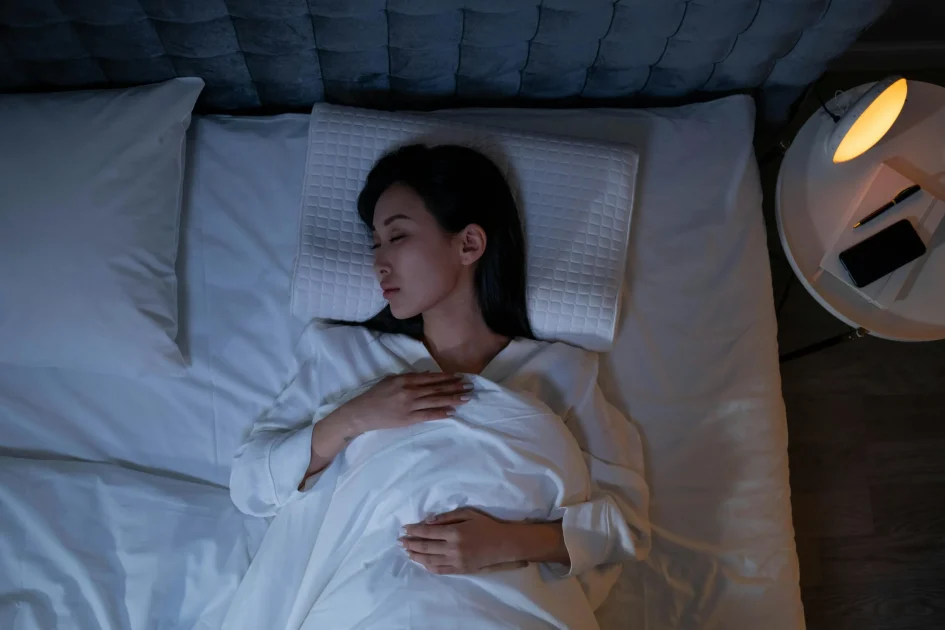 Woman sleeping peacefully in bed at night beside a lamp and phone, representing rest and dreaming