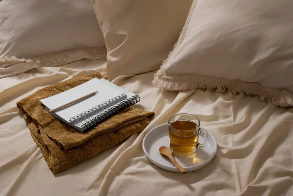 Notebook and tea on a cozy bed, representing journaling, reflection, and a calming bedtime routine
