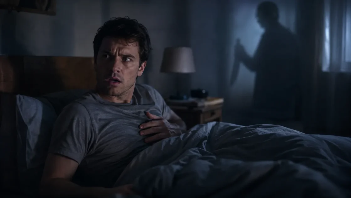 Startled man wakes from a dream of being stabbed but not dying as a shadowy attacker appears behind him.